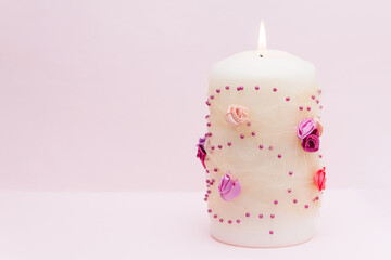 Burning candle with flowers decor on the pink background.