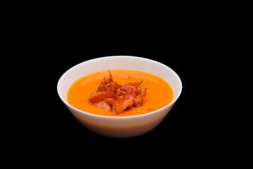 Pumpkin cream soup with bacon in white bowl on dark background