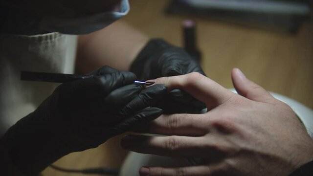 Male manicure - the nail master drawing a minimalistic design using black acrylic nail paint