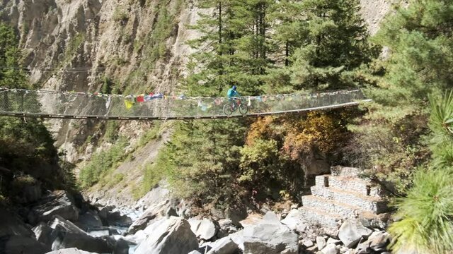 Sherpas and hikers walk a bridge crossing a valley. 