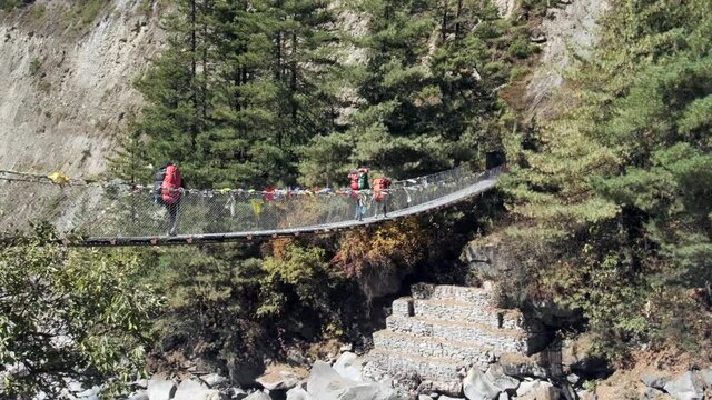Sherpas and hikers walk a bridge crossing a valley. 