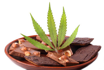 Cannabis leaf with pieces of chocolate with nuts on a saucer, chocolate with CBD cannabis on a white isolated background. Entertainment drug concept
