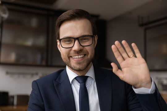 Headshot portrait of smiling young Caucasian businessman wave at camera talk on video call. Profile picture of happy male director have webcam digital virtual conference. Online communication concept.