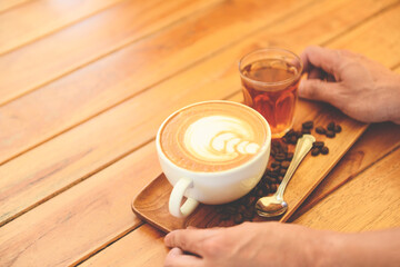 Coffee cup in hand on wooden table in cafe with coffee beans background, Served Coffee Cappuccino or latte.