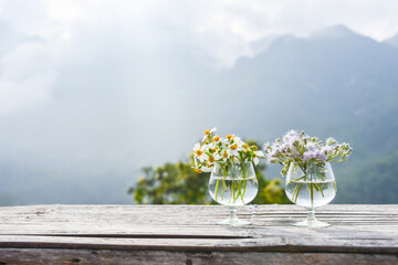 Wild flower in glasses setting on bamboo table with morning hill in mist on background.