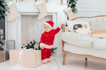 Little child under Christmas tree. baby boy in Santa Claus hat with gifts under Christmas tree with many gift boxes presents