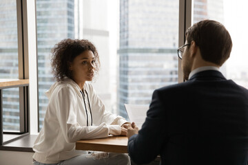 Businessman speak with African American female job candidate at interview in office. Male boss or employer have recruitment talk with biracial woman client or customer at meeting. Employment concept.