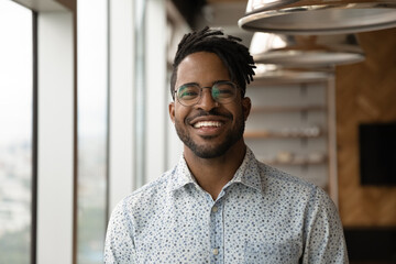 Profile picture of smiling young African American man in glasses pose in own home apartment. Close...