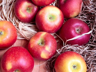 Bright red and yellow apples are stored in hay on a wooden surface