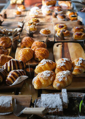 Many fresh bread on a wooden table. Many diverse bread on a wooden board. Variety of breads displayed at bakery shop. Fresh from the oven pastry on wooden table.
