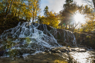 large waterfall and shining bright sun in autumn while hiking