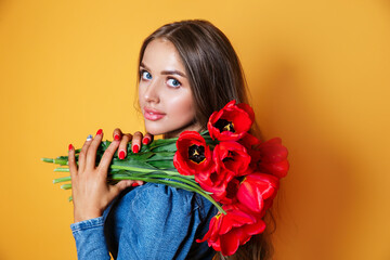 Beautiful woman in the blue dress with red flowers tulips in hands on a yellow background