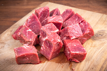Fresh raw beef slices for goulash on wooden kitchen cutting board