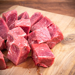 Fresh raw beef slices for goulash on wooden kitchen cutting board