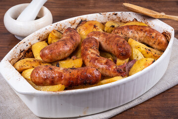 Baked golden potato slices with turkey sausages in a white ceramic baking dish on a wooden table