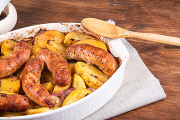 Baked golden potato slices with turkey sausages in a white ceramic baking dish on a wooden table