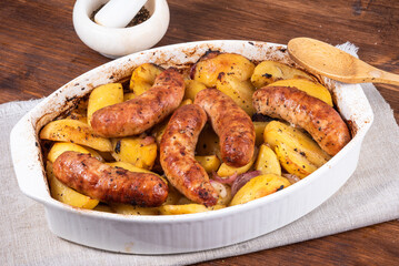 Baked golden potato slices with turkey sausages in a white ceramic baking dish on a wooden table