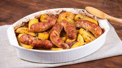 Baked golden potato slices with turkey sausages in a white ceramic baking dish on a wooden table