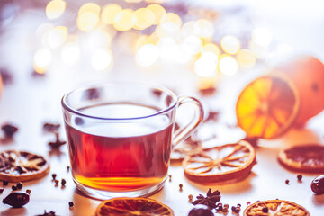 Glass cup of hot aromatic tea on white background with spices. Christmas tea with oranges on bokeh lights background. Christmas tea.	