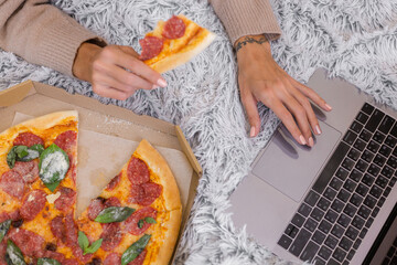 Woman east fast food from delivery on bed in bedroom at home at christmas new year time. Female alone enjoying fat food, pizza. Hungry for carbs.
 