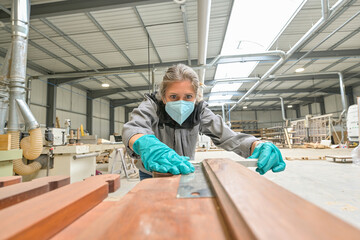 Woman worker operating in the carpentry workshop  and wearing protections againt covid-19