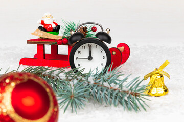 alarm clock, santa claus on a sleigh, a blue spruce branch, a golden bell and a Christmas tree toy ball on a snow background