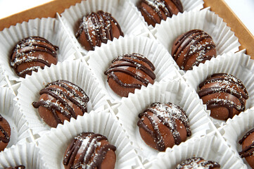 Round dark chocolate candies in a white box close up