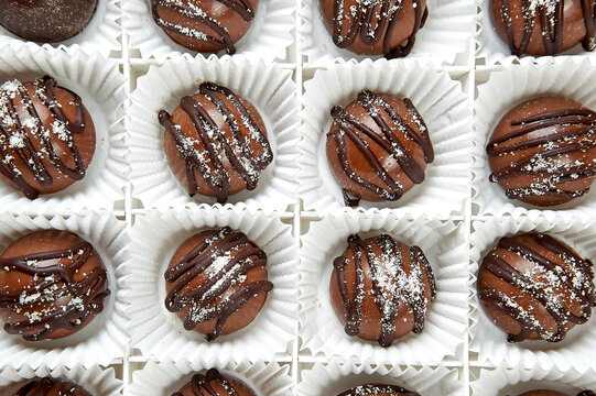 Round dark chocolate candies in a white box close up
