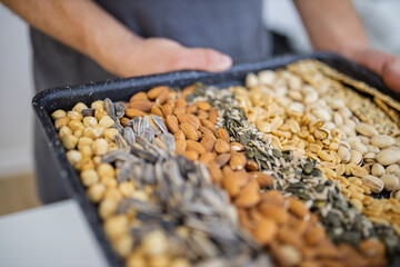 Male hands holding a black tray of nuts and seeds