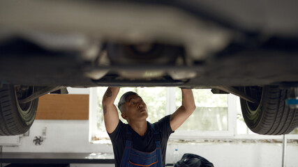 Asian mechanic working under machine at car service station