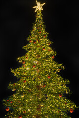 Green Christmas tree with colorful decorations and star on top on dark background.