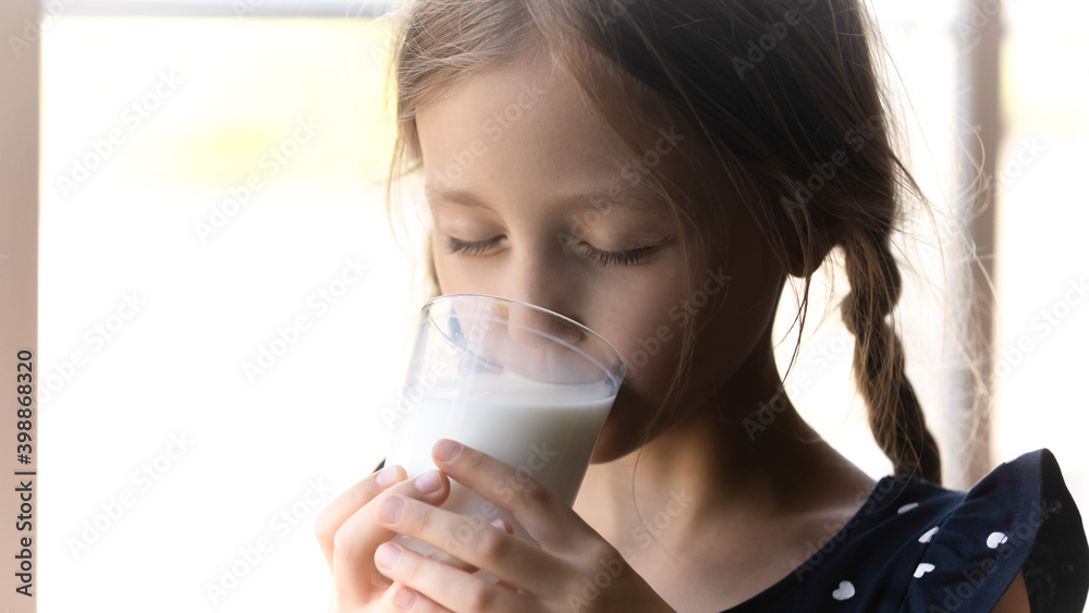 Wall mural close up cute little girl drinking tasty milk, holding glass, pretty preschool child enjoying organi