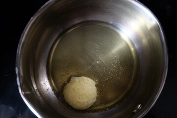 Butter in a pot. One spoon of butter pat melting on an iron frying pan. It is called 