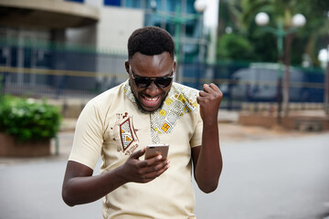 handsome man in the street holding the phone between his hand, he gestures express his joy