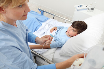 Up view of nurse checking the drip with sick child lying in bed next to her in hospital room