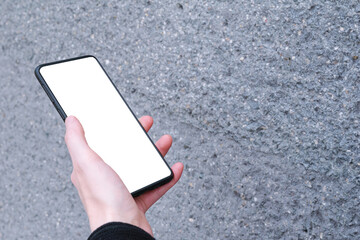 Person's hand holding smartphone with blank white screen mock up on grey background, business 