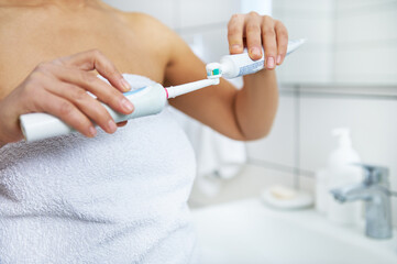 A close-up of the hands of a woman holding a toothbrush in one hand and toothpaste in the other