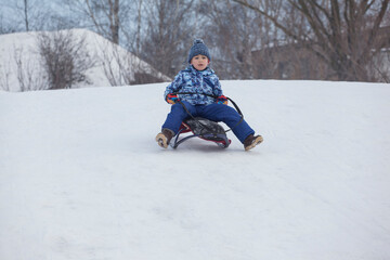 Fototapeta na wymiar little boy riding from a slide on a sleigh