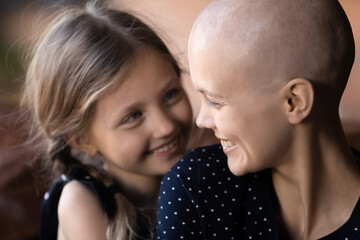 Close up happy cancer patient sick mother and little daughter hugging, laughing, enjoying tender...
