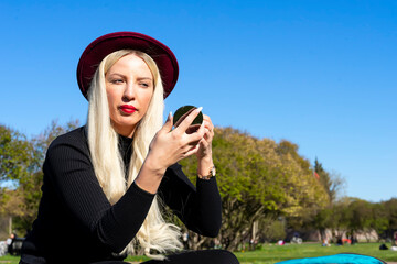 Fototapeta premium A beautiful young woman looks in a mirror against a background of green grass and trees