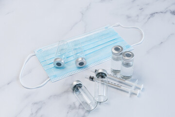 Fototapeta premium Two Full and Two Empty Medical Vaccine Ampules and Two Syringes on Marble Counter top along side one medical face masks..