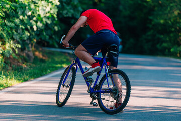 Fit cyclist rides his bicycle (bike) on an empty road in nature wearing a baseball hat and red t-shirt.