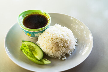Close up of white rice on whhite plate served with a bowl of soup and soy sauce, ready to eat