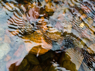 Wavy surface of water on shallow rapid stream with colorful gravel at bottom, running water in creek, intimate landscape