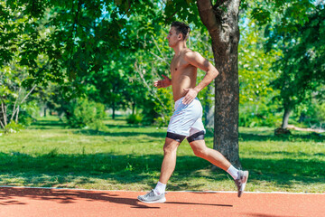 Side view of a strong attractive man running shirtless outside in the park