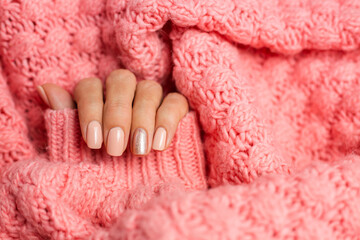 Pretty nude color manicure, one finger shiny golden, on knitted pink wool pillover background  