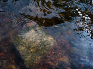 Colorful gravel on bottom of rapid shallow stream visible through clear water, intimate landscape with abstract moving water and underwater pebbles and stone
