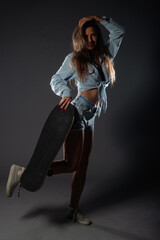 Attractive skater girl posing with her skateboard. Isolated studio photo on a dark background.