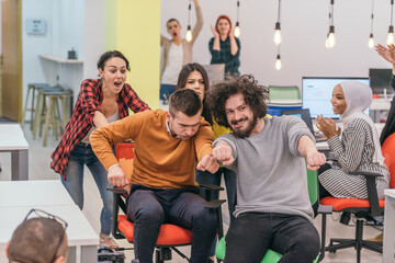 Team building and office fun.Four young cheerful businesspeople in smart casual wear having fun while racing on office chairs and smiling..