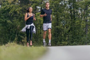 Young fit couple atheltes running on running road in a forest.